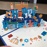 Pop-up card with 'Happy Hanukkah' text and Hanukkah symbols on a white background